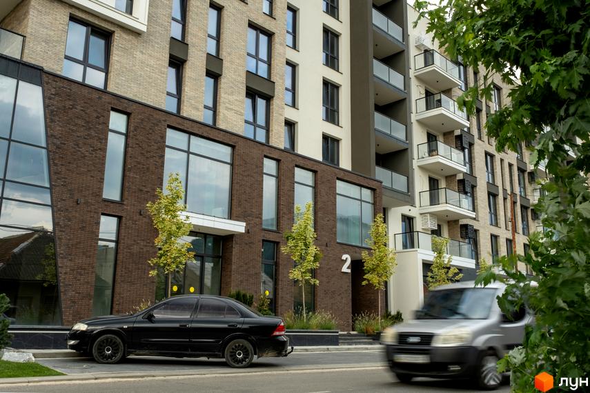 Фасад Житлового комплексу SKY CITY з комбінованою цегляною та світлою обробкою, великими вікнами та балконами. Перед будинком висаджені дерева.