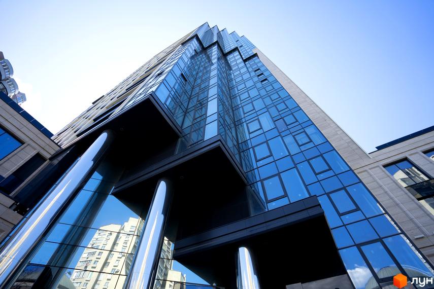 Висотна будівля А136 Highlight Tower зі скляним фасадом, що відбиває небо. Біля основи видно масивні колони та сусідні споруди.