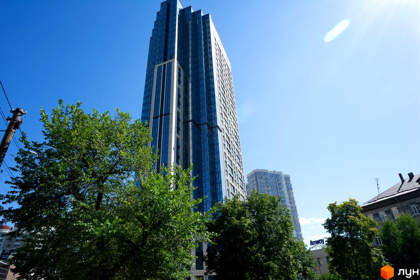 Фасад A136 Highlight Tower зі скла та світлих панелей, оточений густими зеленими деревами на тлі чистого неба.