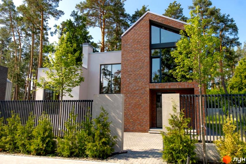 Котеджне містечко At HOME: двоповерховий будинок з цегляним та світлим фасадом, великими вікнами. Прибудинкова територія з огорожею, бруківкою та зеленими насадженнями.