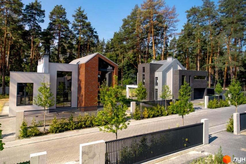 Котеджне містечко КМ At HOME. Сучасні будинки з цегли та штукатурки, огороджені парканом, розташовані серед соснового лісу.