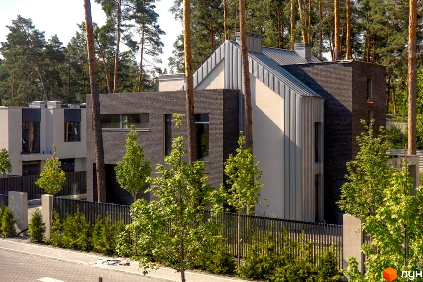 Котеджне містечко At HOME: будинок з темно-сірої цегли та світлих панелей, металевий дах. Навколо зелені дерева та огорожа.