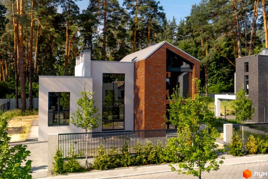 Фасад будинку Котеджного містечка At HOME з цегли та світлої штукатурки, великі вікна. Прибудинкова територія має зелені насадження та огорожу, на фоні сосновий ліс.