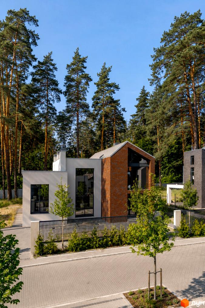 Котеджне містечко At HOME: будинок з фасадом з світлої штукатурки та цегли, великими вікнами. Територія з бруківкою, огорожею та деревами.