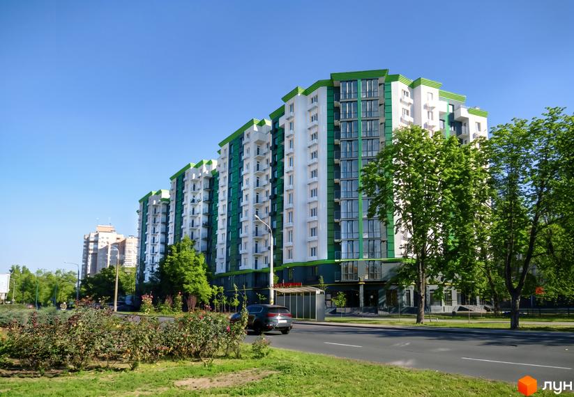 Новобудова Comfort City з біло-зеленим фасадом та балконами, поруч зелені дерева та кущі.