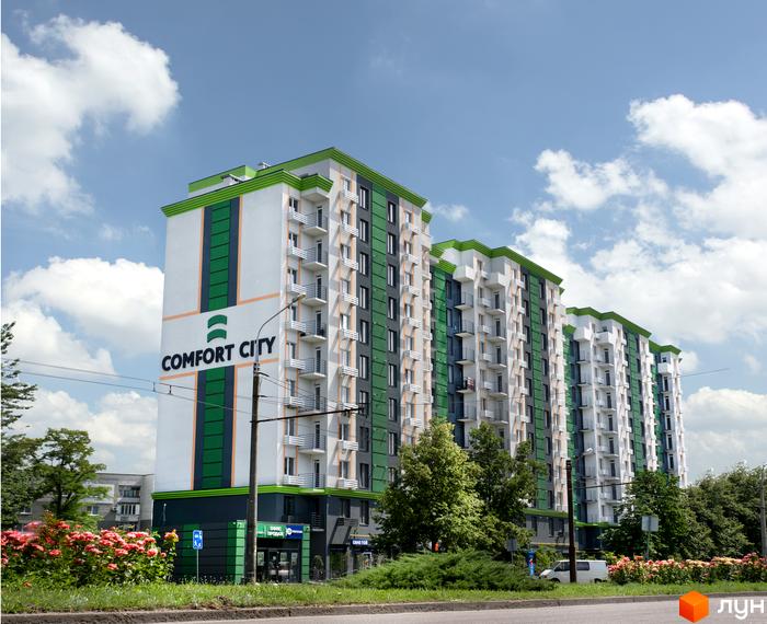 Житловий комплекс Comfort City: багатоповерхові будинки біло-зелено-сірого кольору з балконами, оточені зеленню та квітучими рослинами.