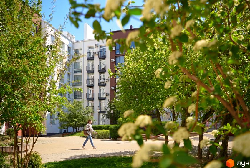 Житловий комплекс Білий Шоколад.Center: білі та коричневі фасади будинків з балконами, зелена прибудинкова територія з деревами та пішохідною доріжкою.