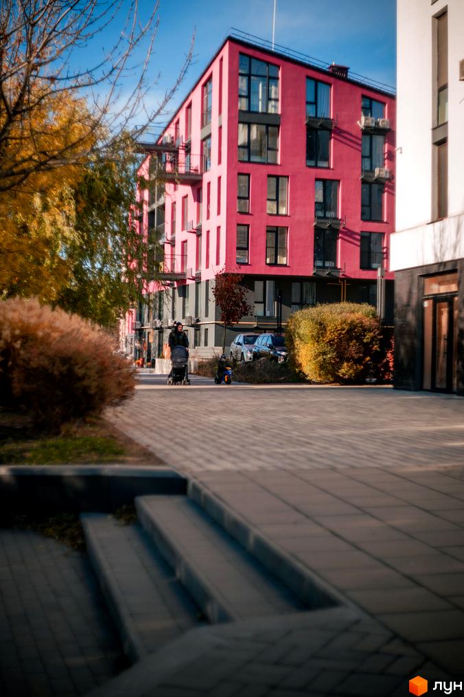 Житловий комплекс City Lake з яскраво-рожевим фасадом та великими вікнами, поруч доглянута прибудинкова територія з деревами та кущами.