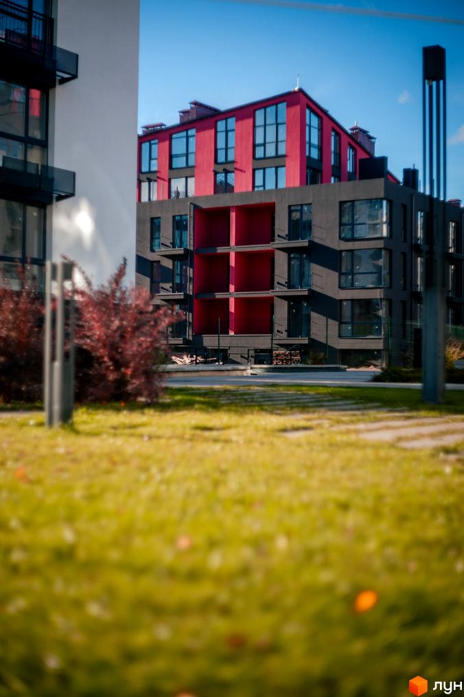 Житловий комплекс City Lake: будинки з темно-сірими та червоними фасадами, великими вікнами. Перед ними зелений газон з осіннім листям.
