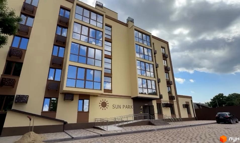 Житловий комплекс Sun Park з бежевим фасадом та великими вікнами. Перед будинком брукована територія з пандусом та сходами.