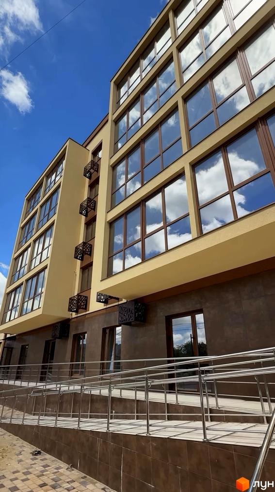 Житловий комплекс Sun Park: багатоповерхова будівля зі світло-коричневим фасадом та великими вікнами. Навколо облаштовано пандус з поручнями.