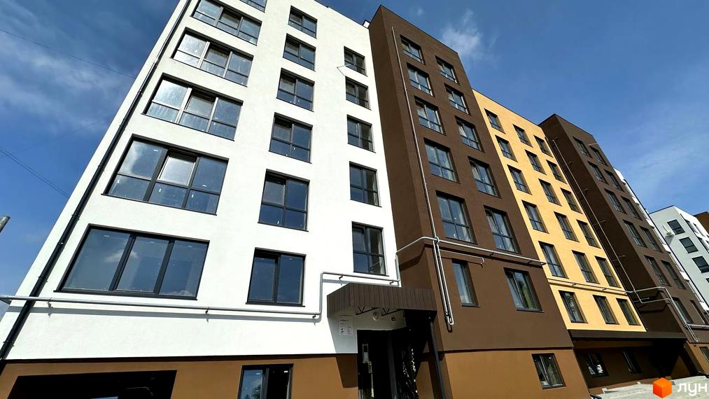 Житловий комплекс PANORAMA DE LUXE: багатоповерхові будинки з фасадами білого, коричневого та жовтого кольорів, з численними вікнами на тлі блакитного неба.