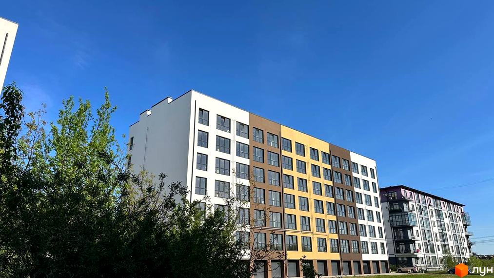 Житловий комплекс PANORAMA DE LUXE: багатоповерховий будинок з білим, коричневим та жовтим фасадом. Поруч зелені насадження та інша новобудова.