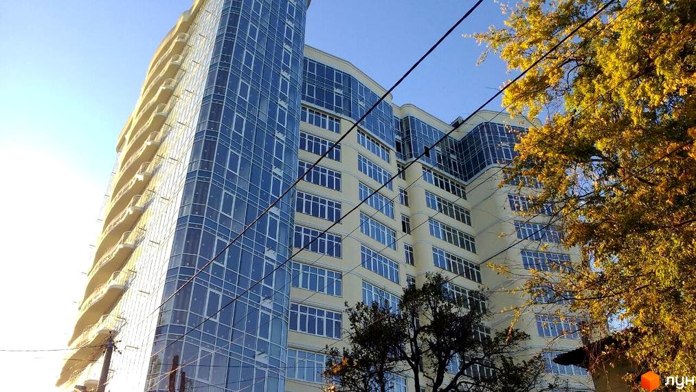 Житловий комплекс Париж: висотна будівля зі скляним фасадом та бежевими стінами з вікнами. Осінні дерева на тлі блакитного неба.