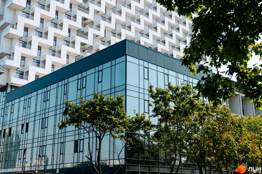 Фасад новобудови BOSTON Creative House з панорамним склінням, біля якого ростуть зелені дерева.