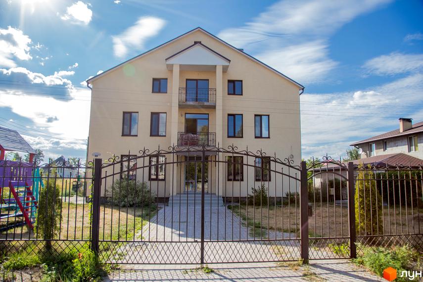 Житловий комплекс Запорізький: світлий будинок з темними вікнами та балконами. На території є огорожа, брукована доріжка та дитячий майданчик.
