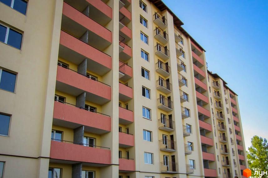 Житловий комплекс на вул. Шевченка, 33 з багатоповерховими секціями, бежевими фасадами та балконами з червоними панелями. Чисте небо.