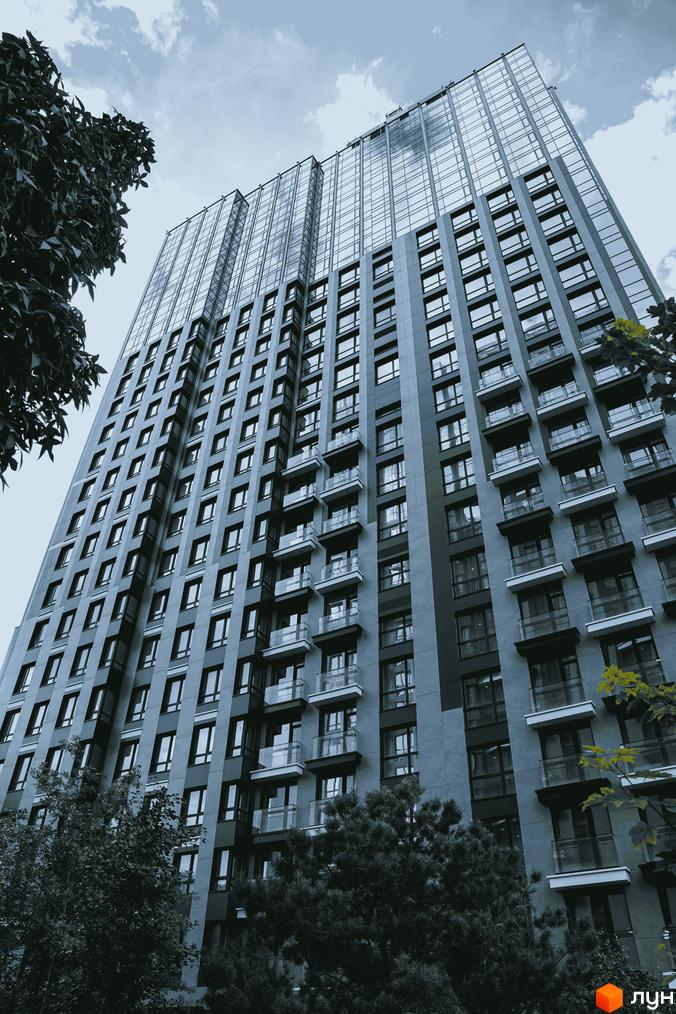 Фасад висотної новобудови EDELDORF HILLS з панорамними вікнами та балконами уздовж стін, біля якої ростуть дерева.