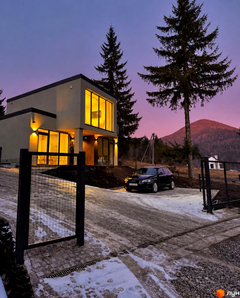 Двоповерховий котедж КМ Solomon Residence з панорамними вікнами, освітленою територією, паркінгом та автомобілем біля гір.