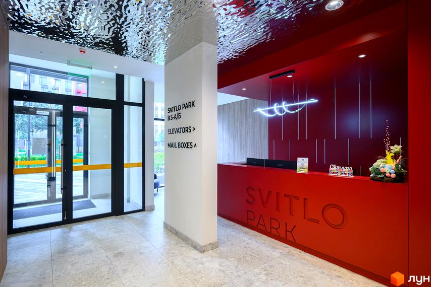 Сучасний холл новобудови Svitlo Park з червоною стійкою ресепшн та великим скляним входом.