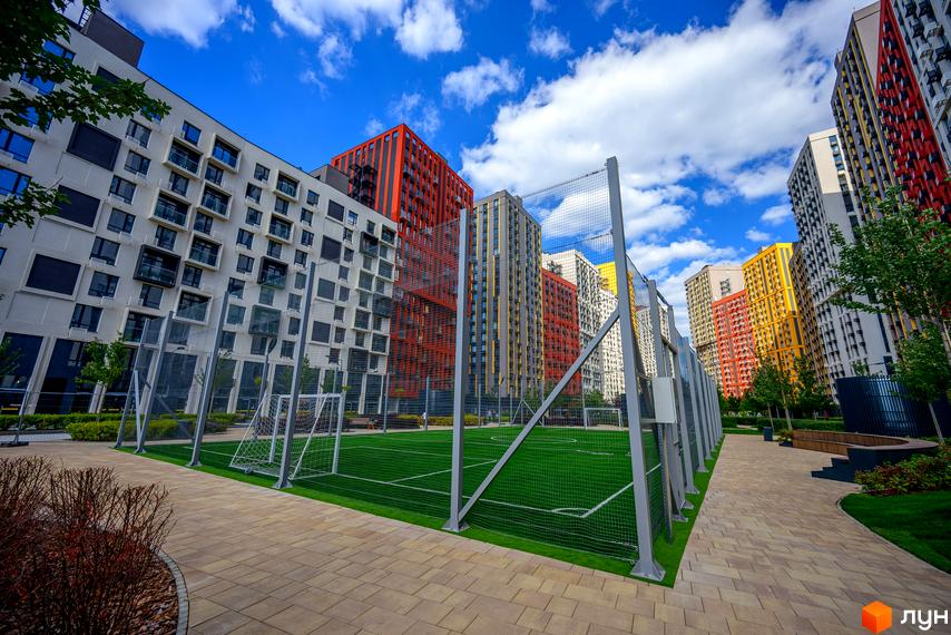 Багатоповерхові будинки яскравих кольорів у ЖК Svitlo Park та футбольне поле на прибудинковій території.