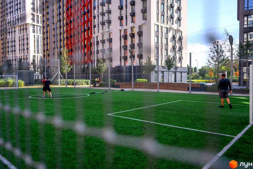 Багатоповерхові будинки ЖК Svitlo Park з контрастними помаранчевими акцентами на фасадній частині та зелений спортивний майданчик.