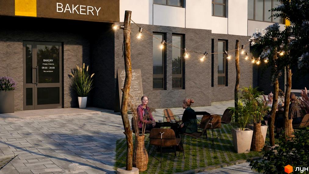 Фасад новобудови із темного каменю з вивіскою BAKERY, а перед будівлею розташована облаштована прибудинкова територія ЖК Зоря 2 з літнім майданчиком.