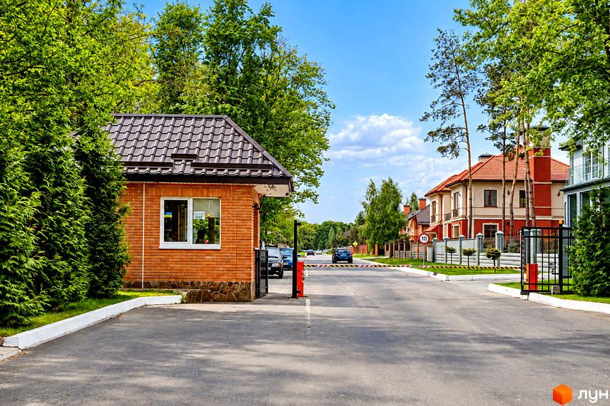 КПП з цегли та темним дахом у котеджному містечку КМ Park House, дорога і зелені дерева вздовж території.