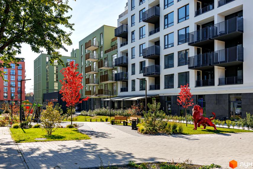 Новобудова ЖК HYGGE LUX з яскравими фасадами та балконами, упорядкована прибудинкова територія з деревами та скульптурою лева.