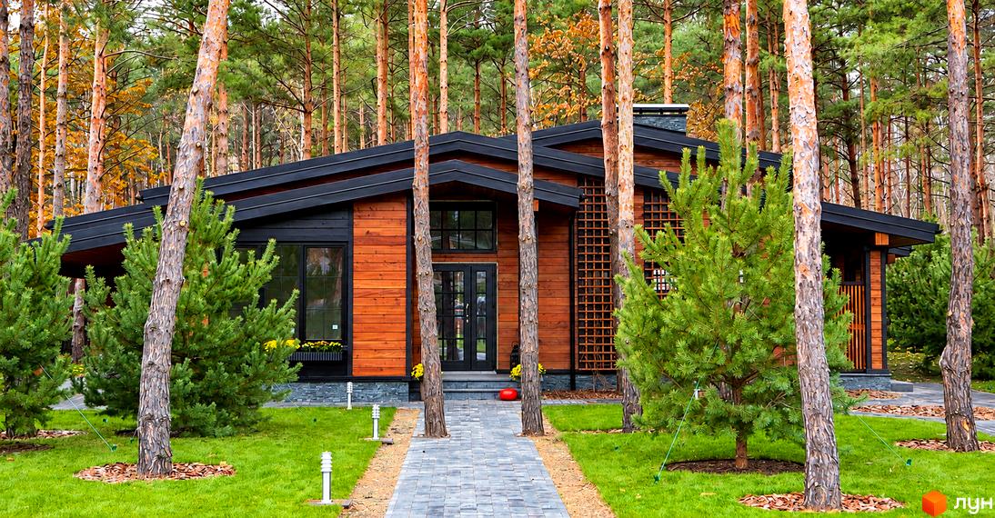 Котеджне містечко Riviera Village: дерев'яний будинок з чорним дахом та зеленою галявиною з соснами.