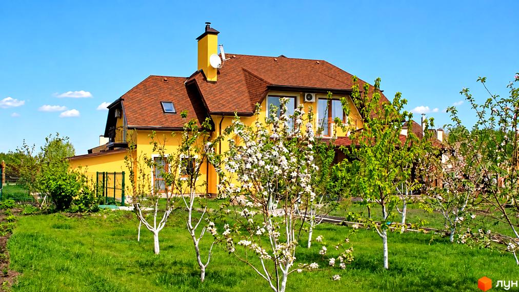 Двоповерховий жовтий котедж КМ Swiss Village з коричневим дахом та зеленим газоном.