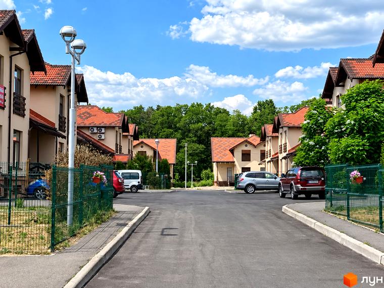Двоповерхові будинки з червоними дахами та асфальтований двір у КМ Садок Вишневий.