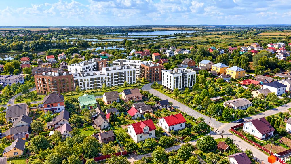 Новобудова Парус LAKE з білими і цегляними фасадами серед зеленої прибудинкової території з ландшафтним дизайном і озером.