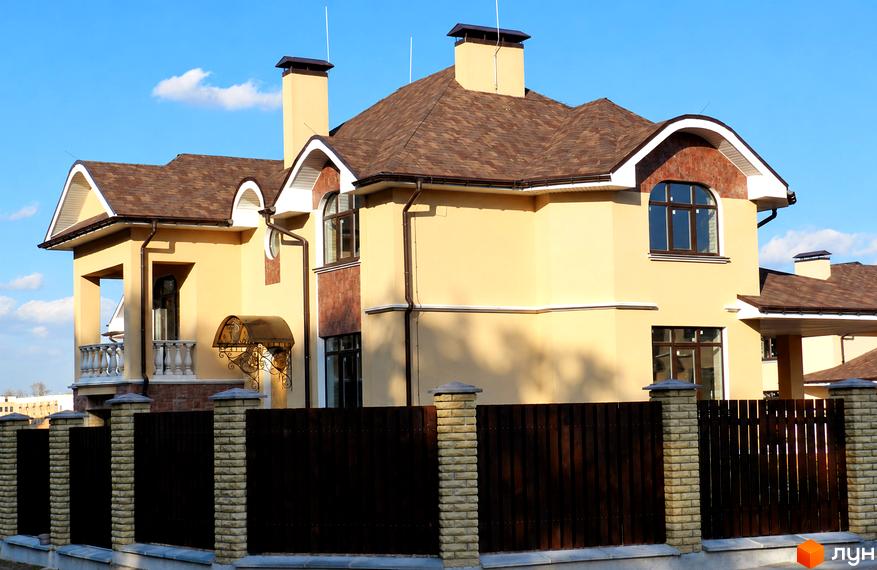 Двоповерховий будинок котеджного містечка КМ FEOFANIA COTTAGE з коричневим дахом та парканом.