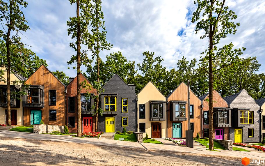 Фасади таунхаусів у КМ Oak Grove Town з різнокольоровими дверима, плиткою та деревом уздовж доріжки.