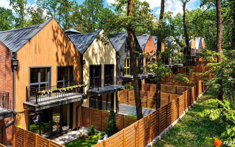 Фасад котеджного містечка КМ Oak Grove Town з дерев'яним облицюванням, балконами та невеликими закритими подвір'ями за парканом.