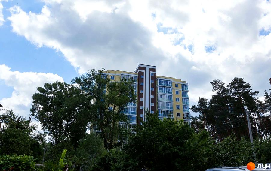 Житловий комплекс Полтавський - жовта багатоповерхівка з коричневою вертикальною вставкою та скляними балконами, оточена зеленню дерев.