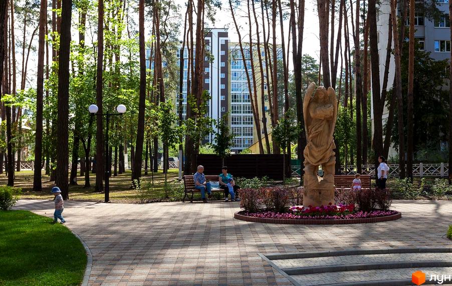 Житловий комплекс Полтавський: багатоповерховий будинок з панорамними вікнами, оточений соснами та парковою зоною зі скульптурою ангела.