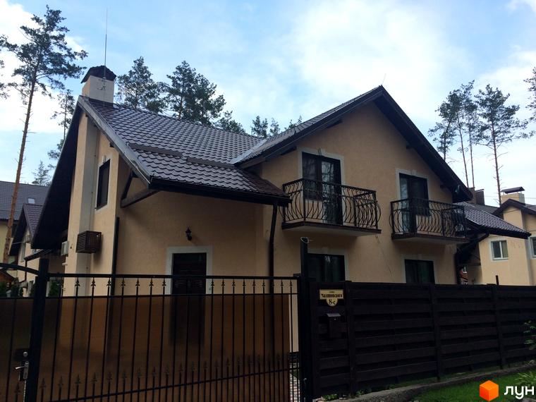 Двоповерховий будинок з коричневим дахом та балконами на другому поверсі, огороджений парканом. Зовнішній вигляд будинку на вулиці Патона.