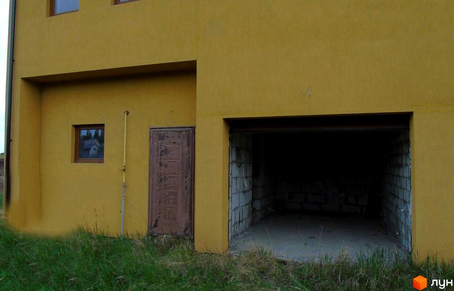 Зовнішній вигляд будинку житлового комплексу Петрівський з гаражним отвором та дверима. Навколо будинку зелена трава.