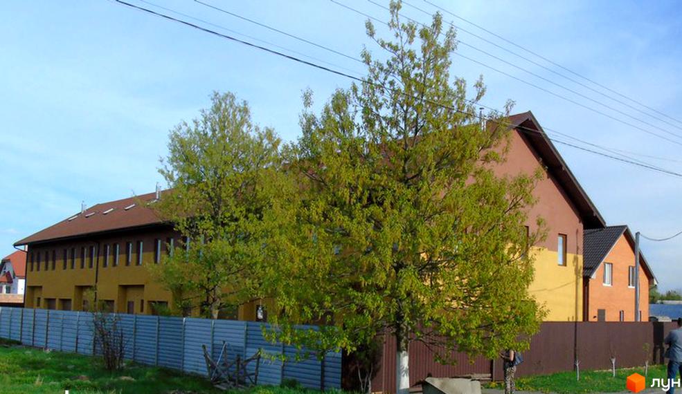 Зовнішній вигляд житлового комплексу Townhouse Петрівський з фасадом жовтого та коричневого кольорів. Навколо комплексу розташована огорожа та дерева.