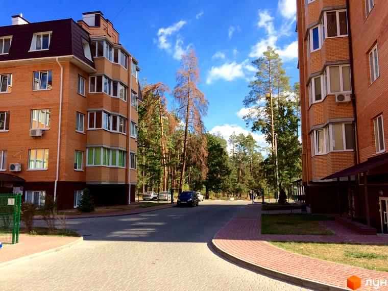 Житловий комплекс Південний. Фасад будинку з цегли, вікна з зеленими рамами, прибудинкова територія з бруківкою та деревами.