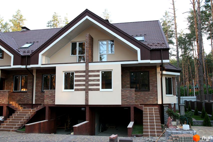 Фасад новобудови на вул. Гоголя, 12в, з коричневим дахом та оздобленням з каменю. Прибудинкова територія з бруківкою та деревами.