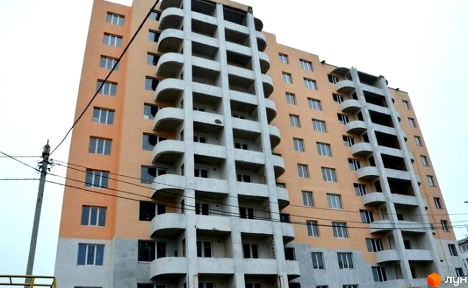 Зовнішній вигляд багатоповерхового будинку житлового комплексу Щасливий з балконами та вікнами. Будівельний проєкт з фасадом персикового кольору.