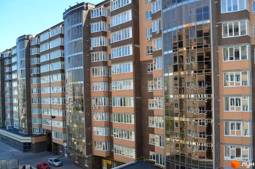 Зовнішній вигляд багатоповерхового будинку ЖК Набережний квартал з панорамним склінням та цегляними вставками. На прибудинковій території видно автомобілі та елементи благоустрою.