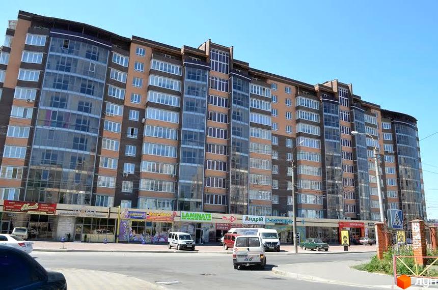 Вид на багатоповерховий житловий комплекс Набережний квартал з фасадом з коричневої цегли та великою кількістю скління. Перед будинком розташована дорога з автомобілями та тротуар.