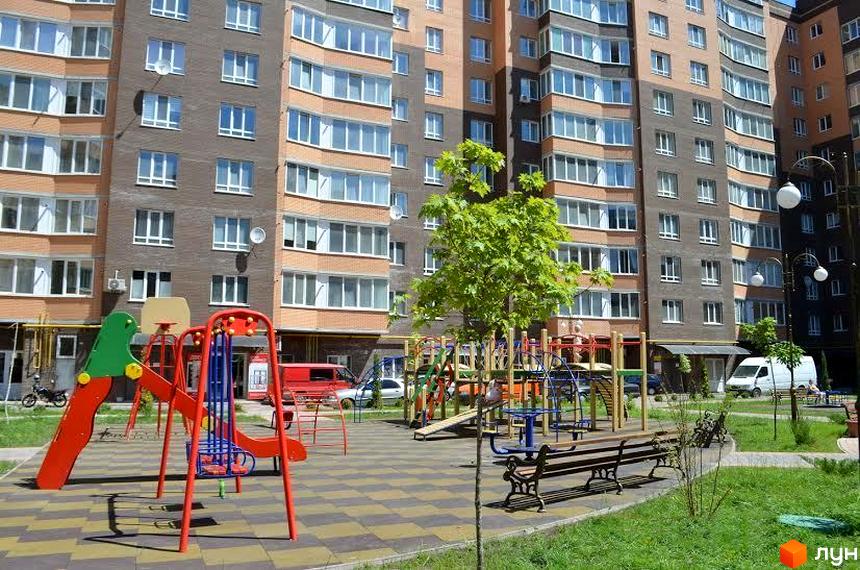 Житловий комплекс Набережний квартал: багатоповерхові будинки з цегляним та сірим фасадом, вікна з білими рамами. Прибудинкова територія з дитячим майданчиком, лавками та деревами.