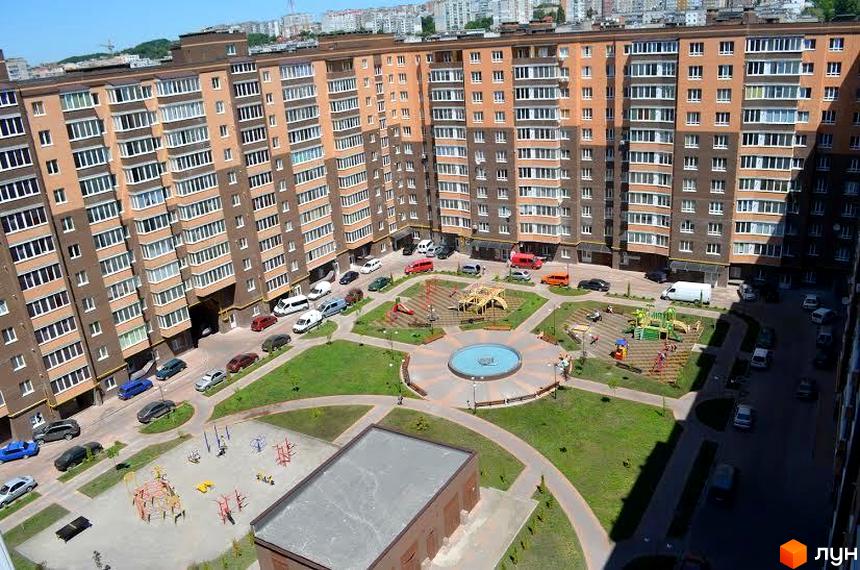 Зовнішній вигляд багатоквартирного будинку ЖК Набережний квартал з коричнево-бежевим фасадом та численними вікнами. На прибудинковій території розташовані дитячі майданчики та зелені зони.