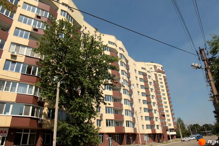 Зовнішній вигляд житлового комплексу Олександрівський посад з балконами та вікнами. Навколо будинку зелені дерева та блакитне небо.