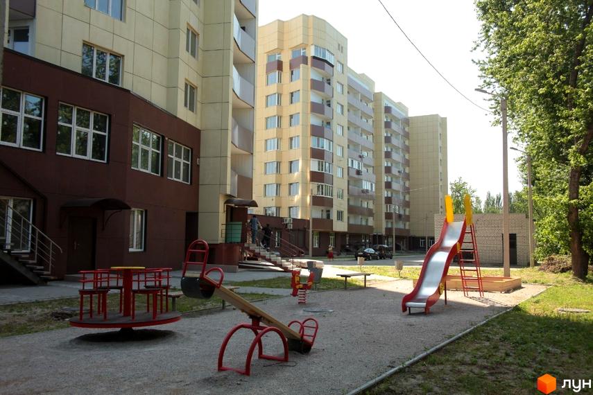 Житловий комплекс Олександрівський посад: багатоповерхові будинки з балконами та дитячий майданчик з гіркою та гойдалками.
